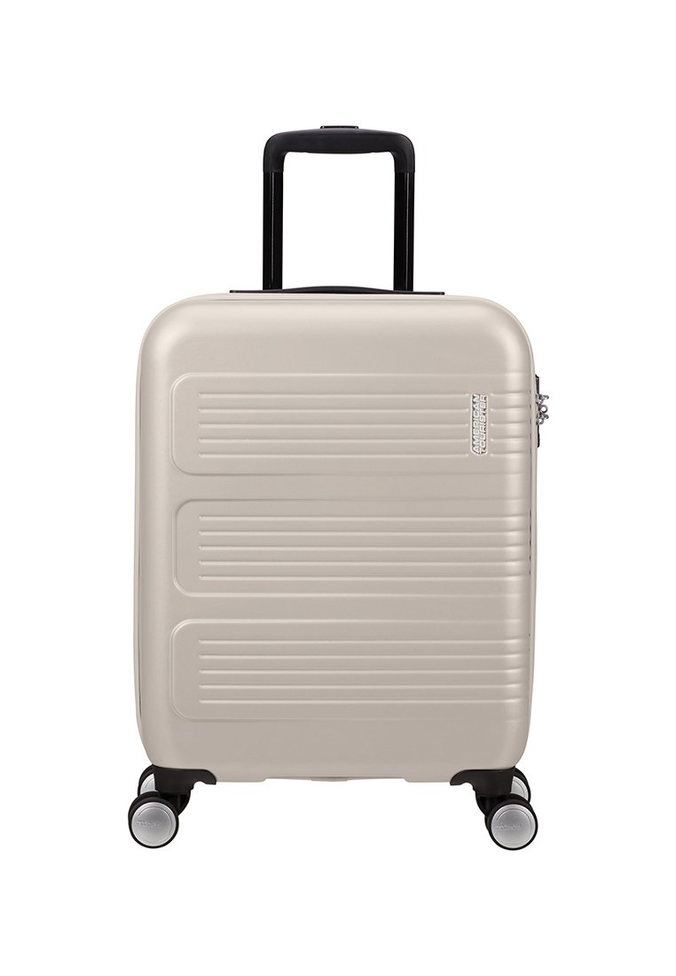 Valise rigide de couleur beige clair avec des rainures horizontales. Elle est dotée d'une poignée noire rétractable et de quatre roues pivotantes pour une maniabilité facile.