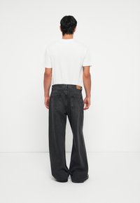 Jean large gris foncé avec une finition texturée et deux poches arrière, associé à un t-shirt blanc uni. Vue arrière de la tenue.