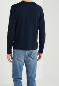 Granatowa koszulka z długim rękawem i okrągłym dekoltem wykonana z miękkiej bawełny, o luźnym kroju i ściągaczach na mankietach, zestawiona z jasnoniebieskimi dżinsami.