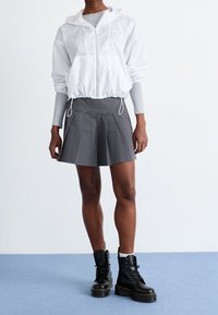 Biała krótka kurtka z kapturem, szara plisowana spódnica i czarne sznurowane buty. Elementy wyróżniające to elastyczne mankiety i sznurek w talii.