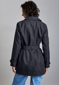 Czarny płaszcz trench z paskiem w talii, długimi rękawami i klasycznym kołnierzem; gładki materiał; stylizowany z jasnoniebieskimi dżinsami.