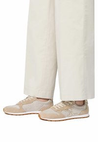 Sneaker beige con un mix di materiali in mesh e suede, con un design testurizzato e suola bianca. Abbinati a pantaloni larghi beige chiaro.