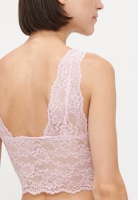 Lys rosa blonde bralette med blomsterdesign, brede blonderstropper og bølget kant. Designet for komfort og støtte.