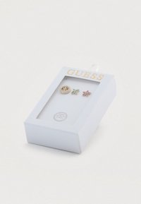 Τρία ζευγάρια σκουλαρίκια εκτίθενται σε ένα λευκό κουτί, με χρυσές, τιρκουάζ και ροζ σχεδιάσεις σε διάφορα σχήματα και με διακοσμητικό από στρας.