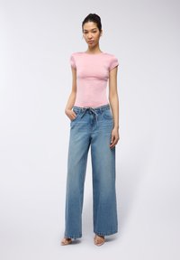 T-shirt aderente rosa, maniche corte; jeans blu in denim a gamba larga con vita regolabile; texture liscia; lavaggio chiaro e silhouette morbida.