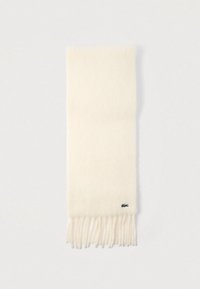 Bufanda color crema hecha de tela suave, con extremos con flecos y un pequeño detalle de logo en un borde. Diseño simple y elegante.