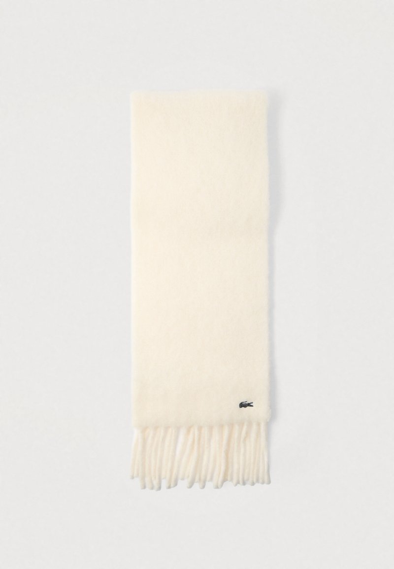 Bufanda color crema hecha de tela suave, con extremos con flecos y un pequeño detalle de logo en un borde. Diseño simple y elegante.