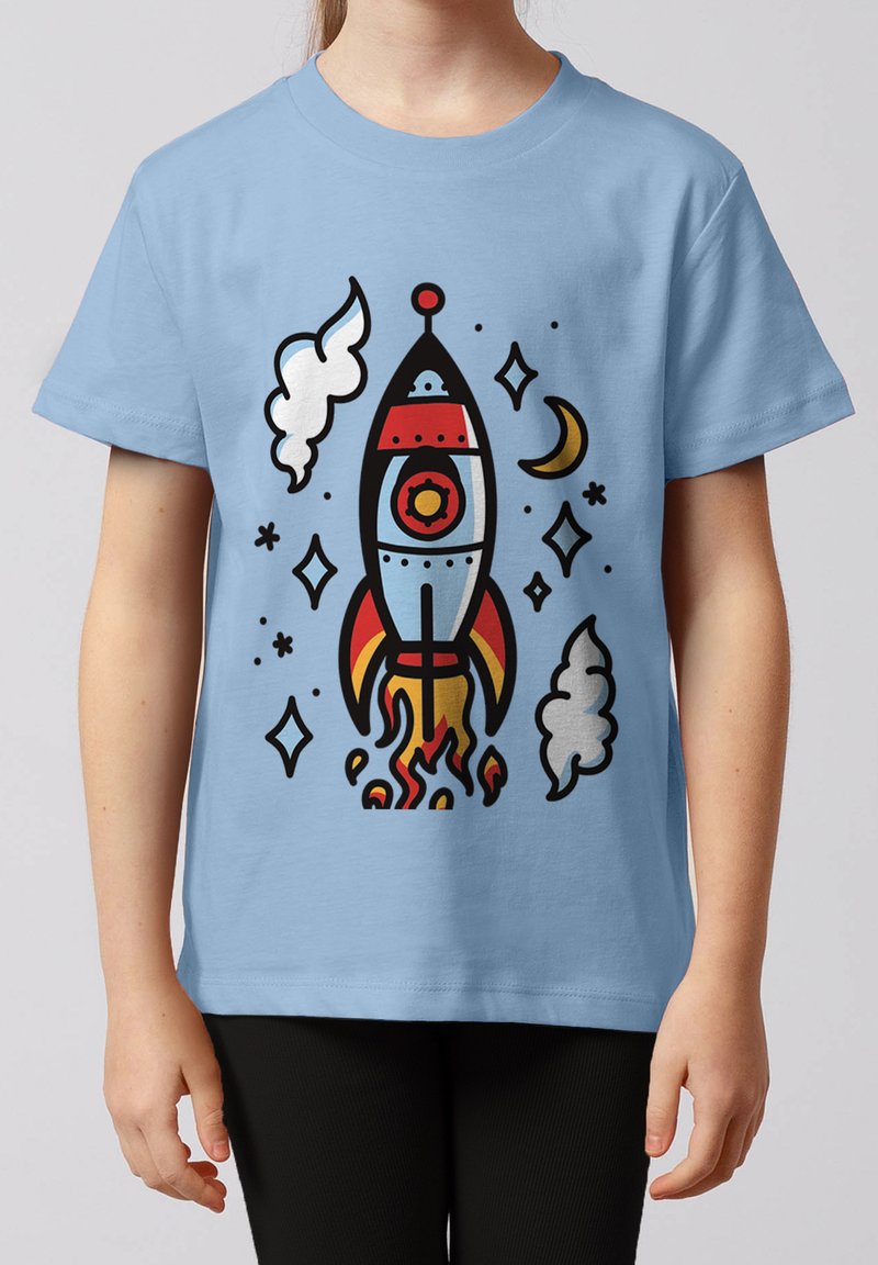 Enfant portant un t-shirt bleu clair avec une fusée de dessin animé colorée en train de décoller, entourée d'étoiles, de nuages de fumée et d'un croissant de lune.