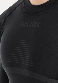 Czarna sportowa koszulka wykonana z gładkiego, elastycznego materiału. Posiada wysoki kołnierz, subtelne logo oraz graficzne detale w jaśniejszym odcieniu.