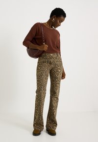 Suéter marrón, pantalones acampanados con estampado de leopardo y calzado marrón. El bolso es de color rojo oscuro con detalles de tachuelas. Joyas sencillas completan el conjunto.