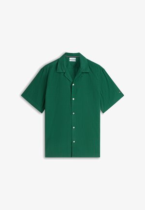 Camisa verde de manga corta con botones, con un sutil estampado de cuadros, cuello campestre y botones blancos, extendida sobre un fondo blanco.