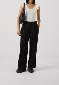 Svarta skräddarsydda byxor med vida ben, i kombination med en vit linne topp med volanger på axelbanden och en svart handväska. Kraftiga svarta skor fulländar looken.