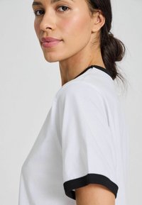 White t-shirt with short sleeves, featuring black ribbed cuffs and neckline. Smooth fabric texture, relaxed fit, and plain design.