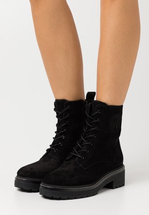 Bottines en suede noir avec des lacets, une pointe ronde et une semelle épaisse noire. Caractéristiques de détails de logo et d'accents de couture.
