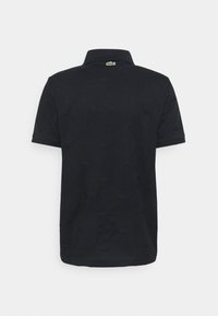 Polo noir avec un tissu texturé, manches courtes et col classique. Un petit logo vert est visible au niveau de l'encolure arrière.