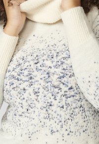 Maglione lavorato a maglia di colore crema con colletto alto, caratterizzato da un motivo a pois blu e grigio e polsini a coste. Texture morbida e vestibilità rilassata.