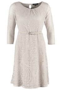 Robe en dentelle beige clair avec manches trois quarts, encolure ronde avec bouton en forme de goutte et une fine ceinture assortie à la taille.