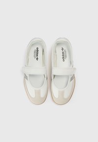 Άσπρα και γκρι παπούτσια Adidas με σχεδιασμό λουριού, ανώτερο μέρος από λείο δέρμα, σουέντ λεπτομέρειες και υφή στη σόλα από καουτσούκ.