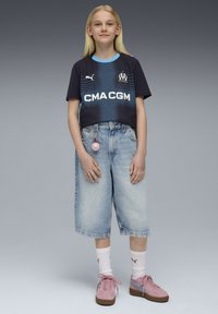 Must musta ja sinine Puma jerser, millel on logo, koos heledate baggy denim lühikeste pükstega. Roosa tossud heledate siniste aktsentidega, valged lühikesed sokid.