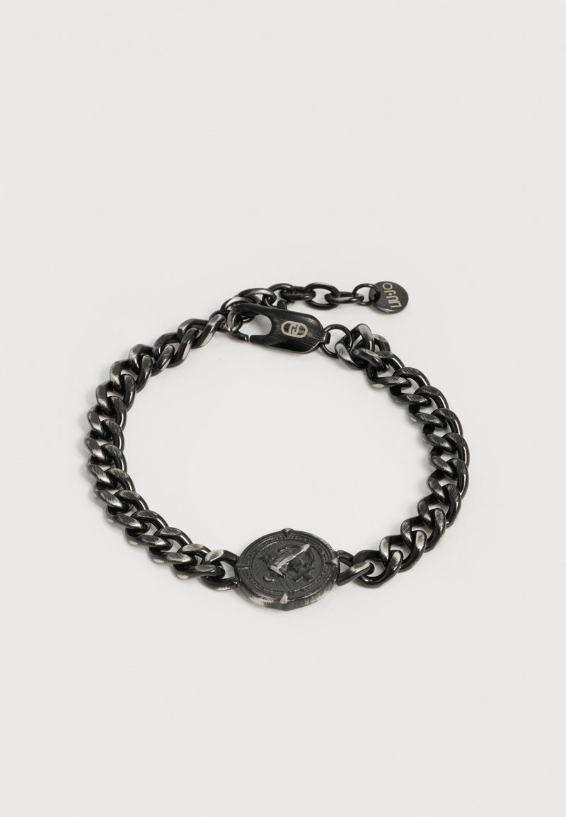 Βραχιόλι με μαύρη μεταλλική αλυσίδα, στρογγυλό εγχάρακτο μενταγιόν κέρματος και κούμπωμα με μοχλό καβουριού, που διαθέτει μικρή ετικέτα μάρκας.