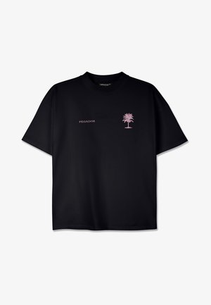 Juodos spalvos trumpomis rankovėmis medvilninis marškinėliai su apvalia iškirpte. Krūtinėje yra rožinės palmių medžio grafika ir rožinės spalvos užrašas "PEGADOR".