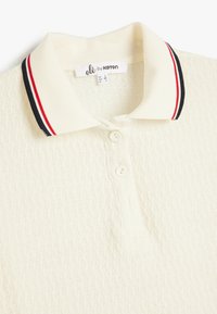 Polo shirt lavorato a maglia color crema con texture a coste, tre bottoni bianchi e colletto con strisce rosse e navy.