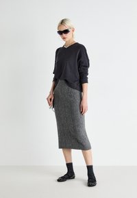Pulover negru cu embellishments, fustă midi tricotată gri cu model texturat și balerini negri cu studuri purtați cu șosete închise la culoare.