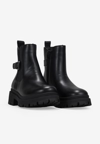 Botas de cuero negras hasta el tobillo con suela gruesa, cremallera lateral y detalle de hebilla decorativa. Textura suave con un diseño elegante y afilado.