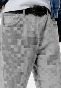 Pantaloni grigi a fantasia con un design pixelato, realizzati in materiale denim, con cuciture a contrasto. Inclusi tasche e una cintura nera.