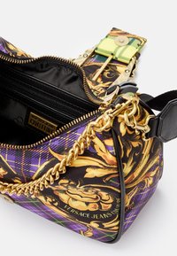 Borsa Versace Jeans Couture con motivo floreale colorato, tracolla in catena dorata, zip nera e dettagli a quadri. Texture liscia e forma compatta.