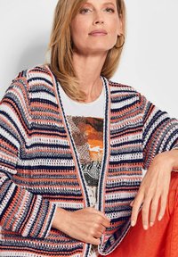 Multicolore gebreide cardigan in oranje, marineblauw en witte strepen, met een open voorkant en losse mouwen. Draag over een patroon top.