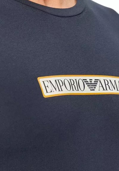 T-shirt blu navy in tessuto morbido con una patch logo bianca e oro che recita "EMPORIO ARMANI" sul petto.