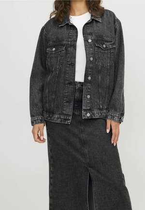 Nainen pukeutuneena mustaan farkkutakkiin, jossa hopeiset napit, valkoisen yläosan päällä ja yhdistettynä vastaavaan mustaan farkkuhameeseen, jossa on etuviilto.