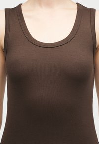 Κοντινή λήψη ενός ατόμου που φορεί αμάνικη, ριγωτή, σκούρα καφέ μπλούζα με στρογγυλή λαιμόκοψη.