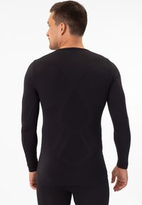 Schwarzes, langärmliges Sportshirt aus strukturiertem, dehnbarem Material. Es verfügt über eine enganliegende Silhouette mit einem geometrischen Muster auf dem Rücken.