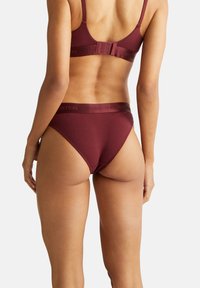 Burgunderfarbene Bralette und passender Bikini-Satz, aus glattem Stoff, mit einem Logo-Band und verstellbaren Trägern, in einem modernen Schnitt.