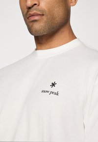 White cotton t-shirt with a crew neckline featuring a black asterisk graphic and the text "snow peak" embroidered on the left chest.