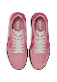 Ténis cor-de-rosa com um upper de tecido texturizado, apresentando atacadores brancos, acentos em chevron cor-de-rosa e uma sola de borracha castanha em contraste.