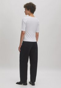 Witte, aansluitende t-shirt met een ronde hals, gecombineerd met zwarte, losse jeans. Model heeft krullend haar en draagt zwarte schoenen.