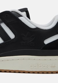 Zwarte leren sneaker met witte strepen, textuurelementen, een gevoerde kraag en een crèmekleurige middenzool met reliëfbranding.