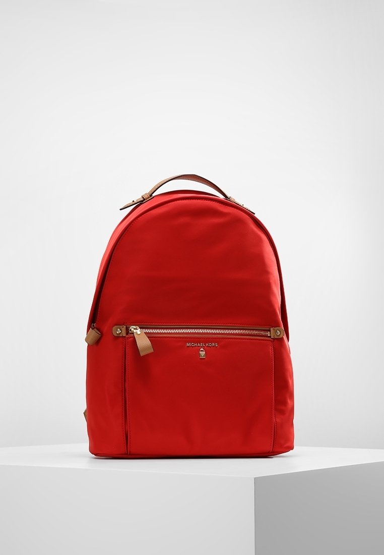 Rød nylon rygsæk med en afrundet form, brune læderdetaljer, en frontlomme med lynlås og guldfarvede metaldetaljer.