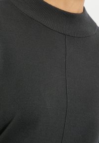 Czarny sweter z dzianiny z prążkowanym kołnierzem, gładką fakturą i dopasowanym krojem z szwem biegnącym wzdłuż środka.
