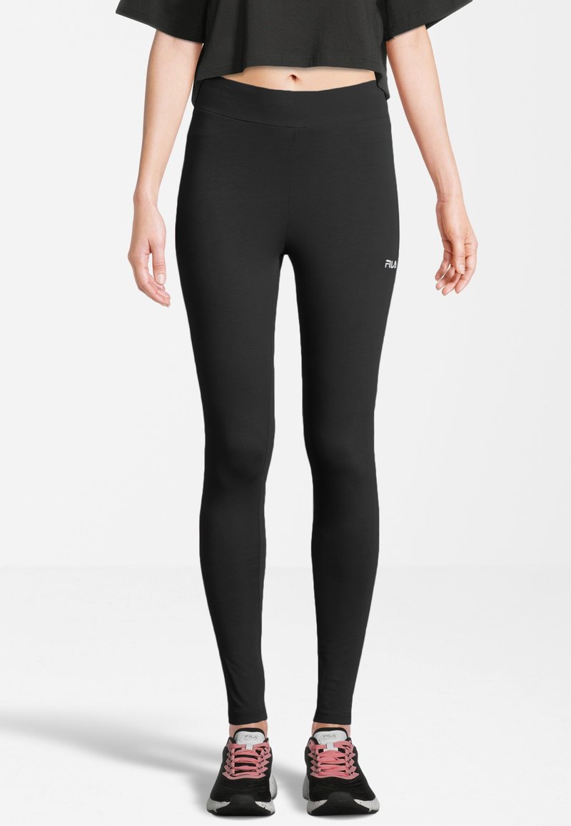 Leggings negros de material elástico, con una cinturilla alta y un pequeño logo en el lado izquierdo, combinados con zapatillas negras y rosas.