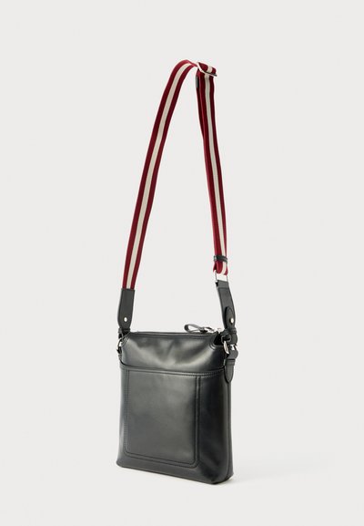 Black leather crossbody bag with front pocket and adjustable red and white striped fabric shoulder strap, set against a plain light background.