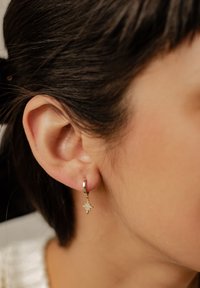 Goldene Creolen mit einem sternförmigen Charm, der mit kleinen Strasssteinen verziert ist und an einem glatten Metallring hängt.