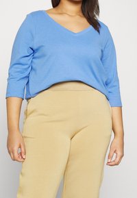 Maglietta azzurra chiara a maniche lunghe con scollatura a V abbinata a pantaloni beige elasticizzati. Tessuto morbido, vestibilità comoda e design rilassato.