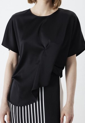 Femme portant un haut noir à manches courtes avec un ourlet asymétrique sur une jupe rayée verticalement noire et blanche.