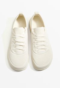 Vita sneakers med övre del av andningsbar mesh, platta snören, dragflik vid hälen och texturerad gummisula. Minimalistisk design, lätt konstruktion.