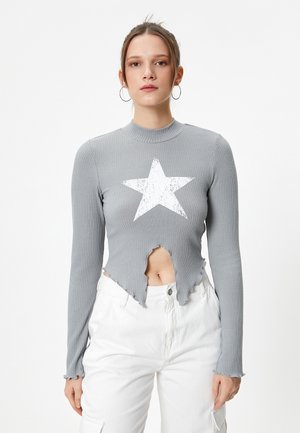 Haut à manches longues gris côtelé avec un ourlet effiloché, un centre découpé et un graphique d'étoile blanche. Associé à un pantalon blanc.