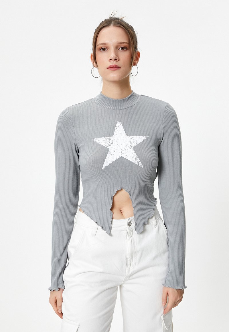 Haut à manches longues gris côtelé avec un ourlet effiloché, un centre découpé et un graphique d'étoile blanche. Associé à un pantalon blanc.
